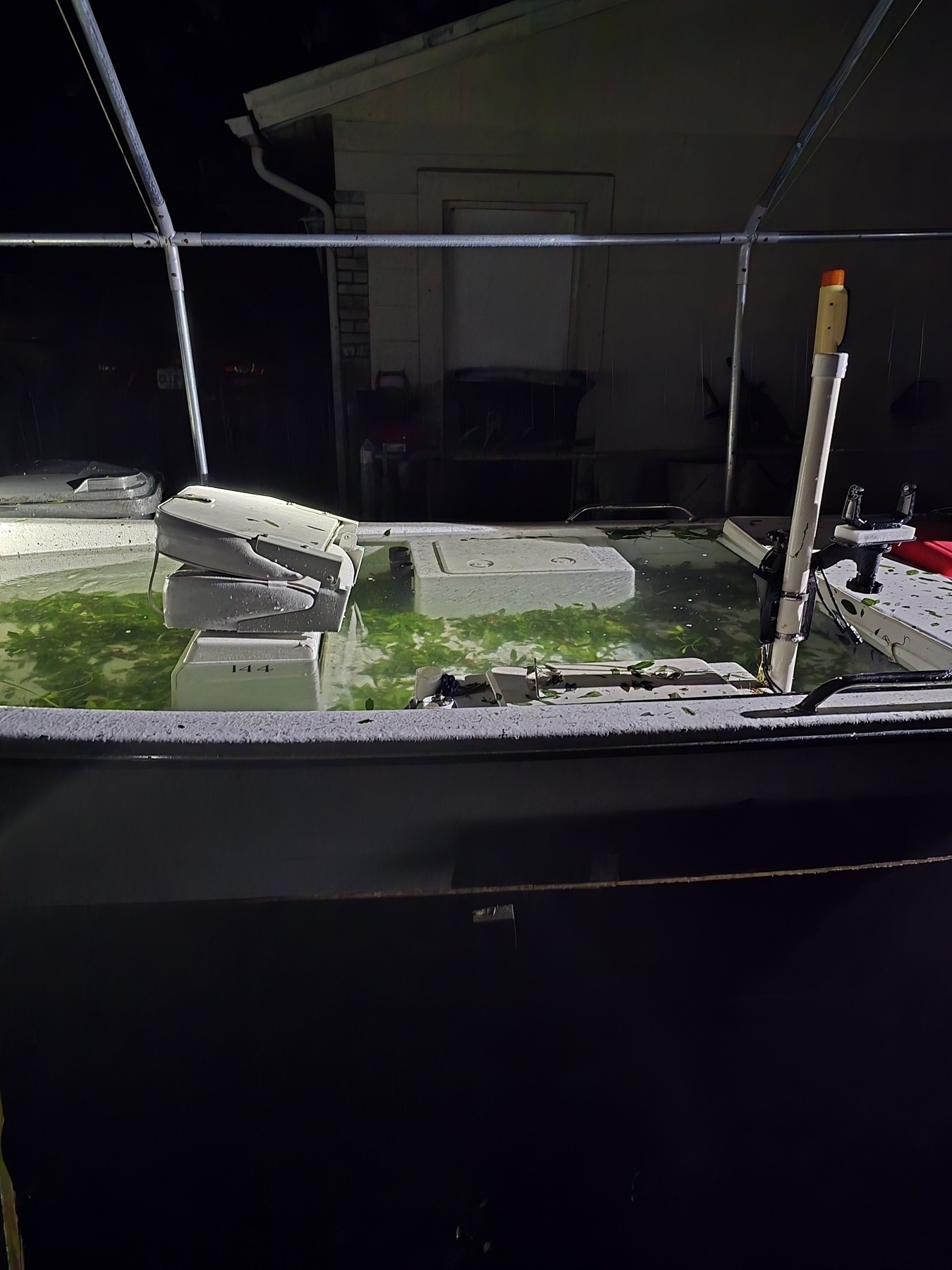 A flooded boat filled with water is seen at night, situated next to a house or building.